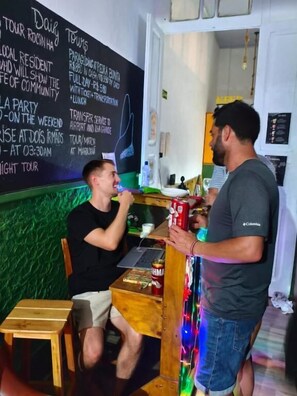 A person seated at a table with a laptop, another person standing beside them, and a chalkboard with text in the background. - Cocos Hostel Rio (Rio de Janeiro)