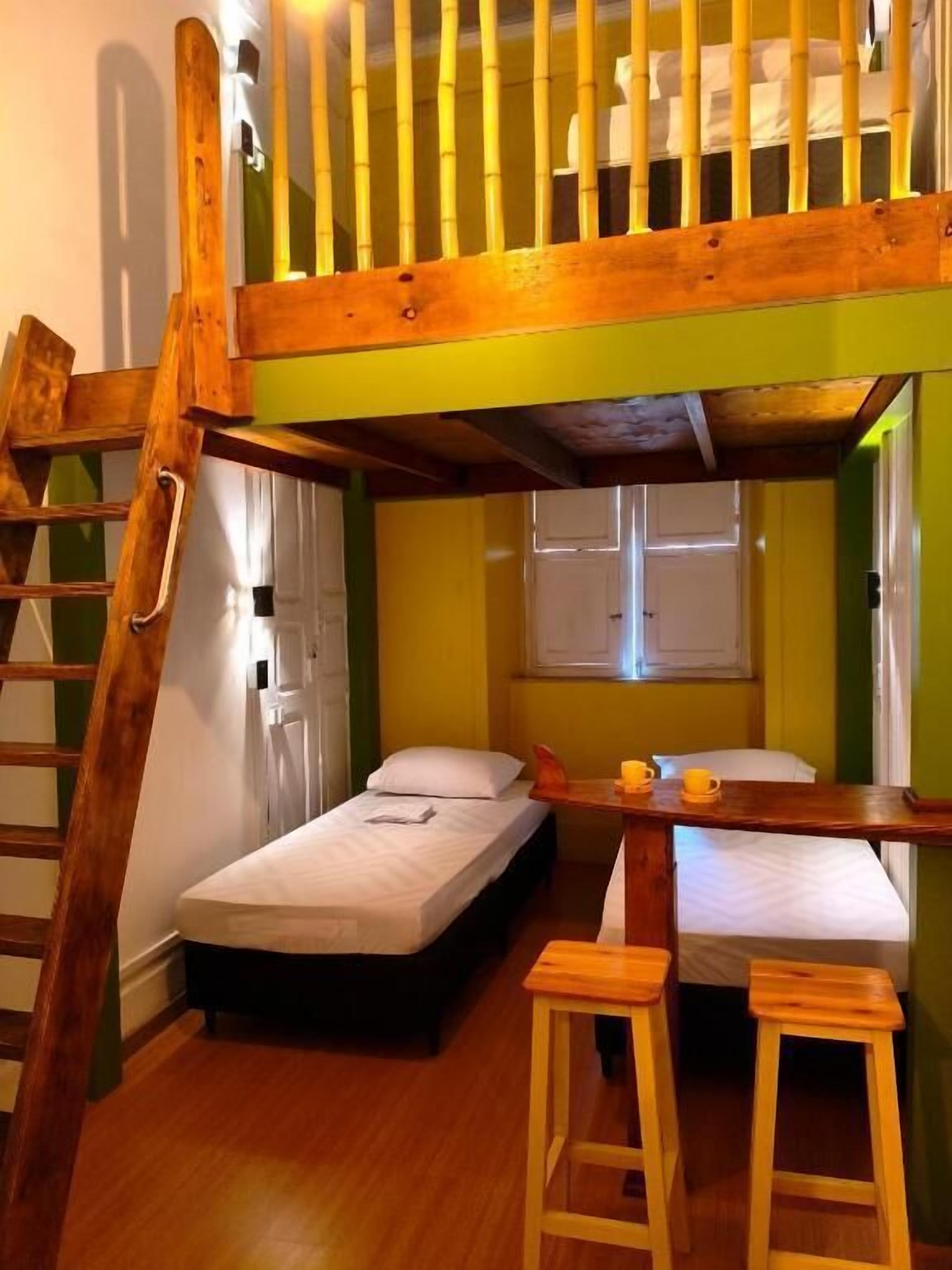 Une chambre avec un lit superposé, une échelle, deux lits simples et une petite table avec des tasses.
