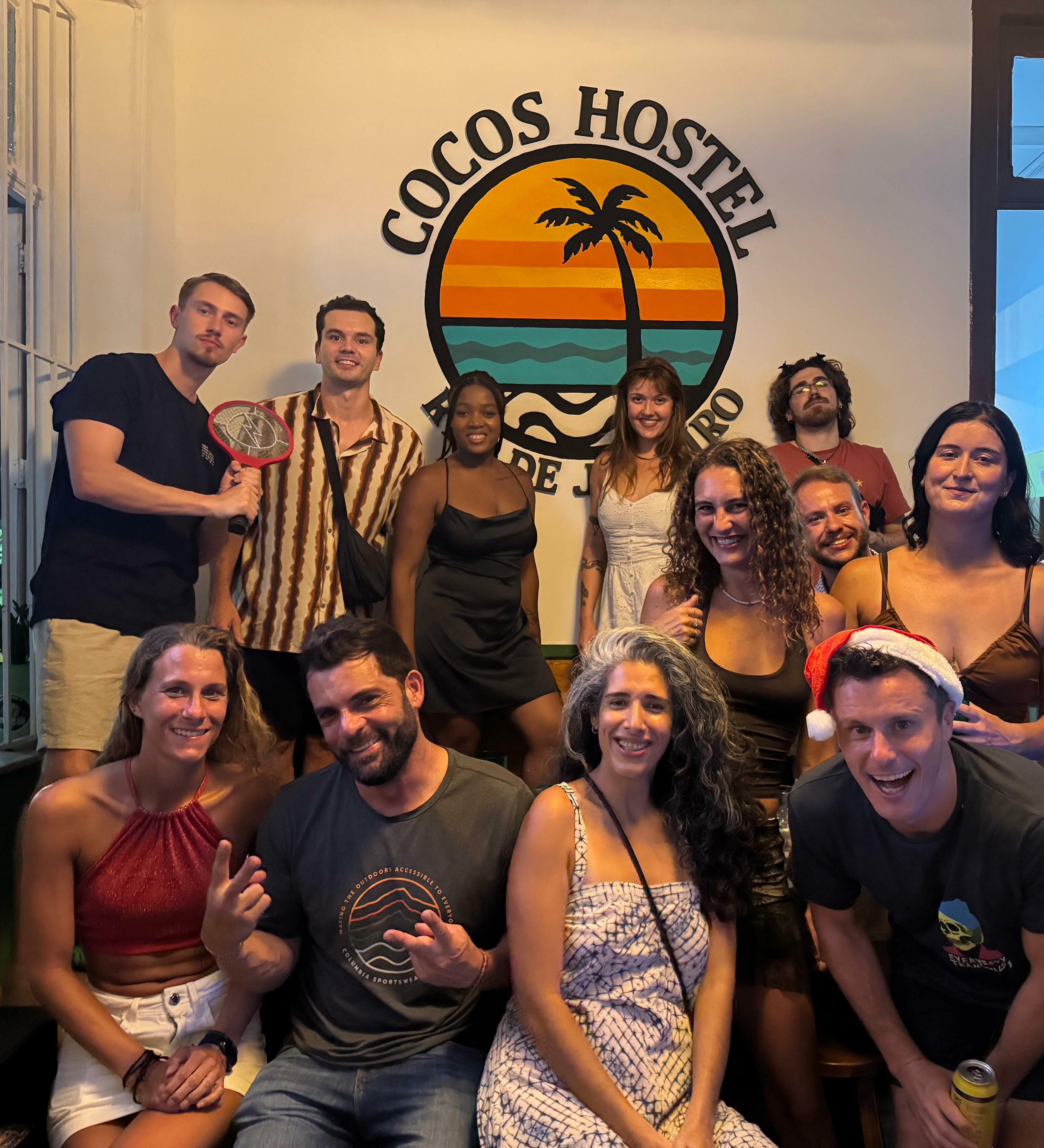 Eine Gruppe von Personen vor einer Wand mit einem Logo, auf dem 'Cocos Hostel' steht.
