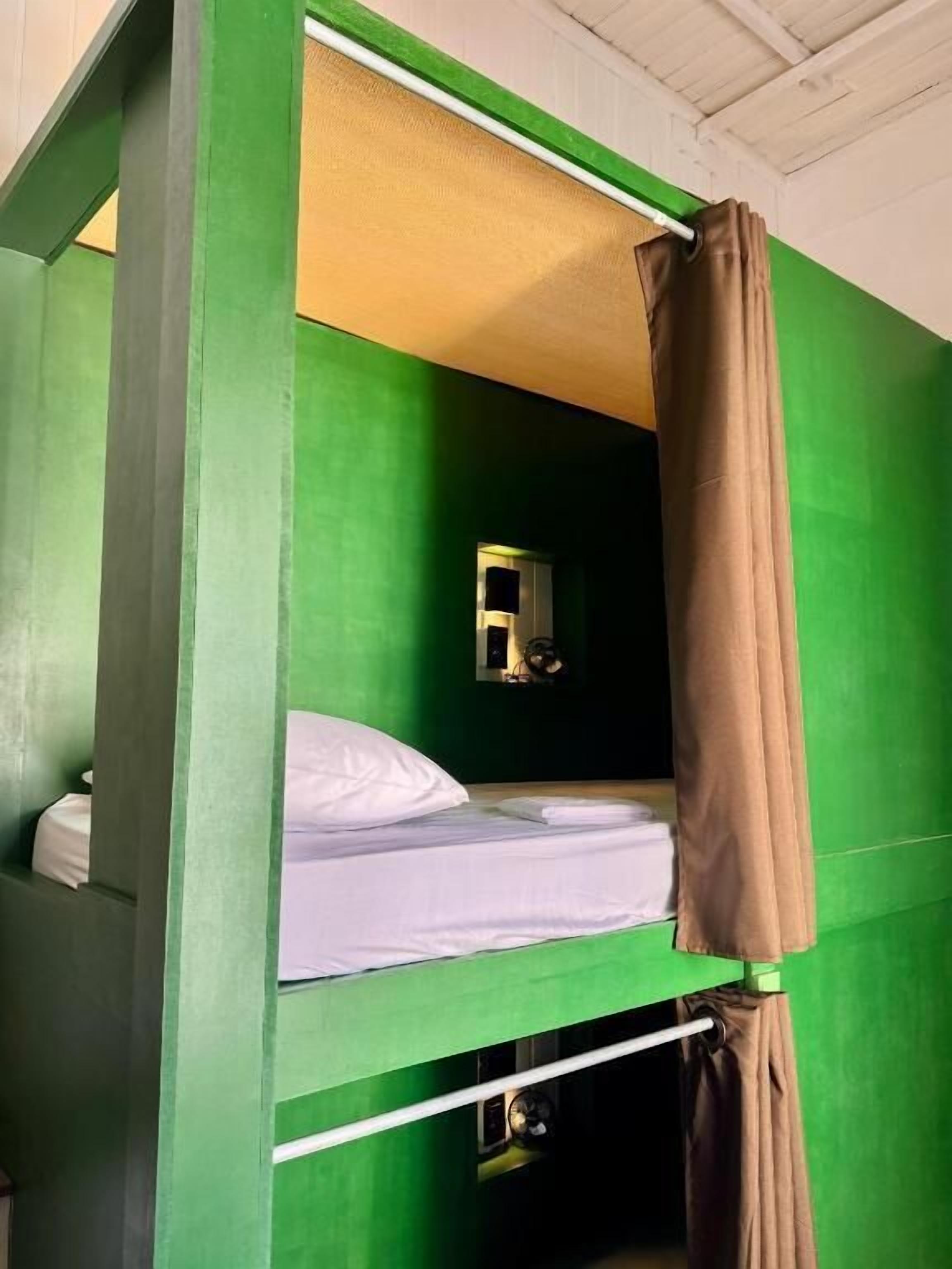 Una cama litera con pared verde, una ventana pequeña y una cortina.