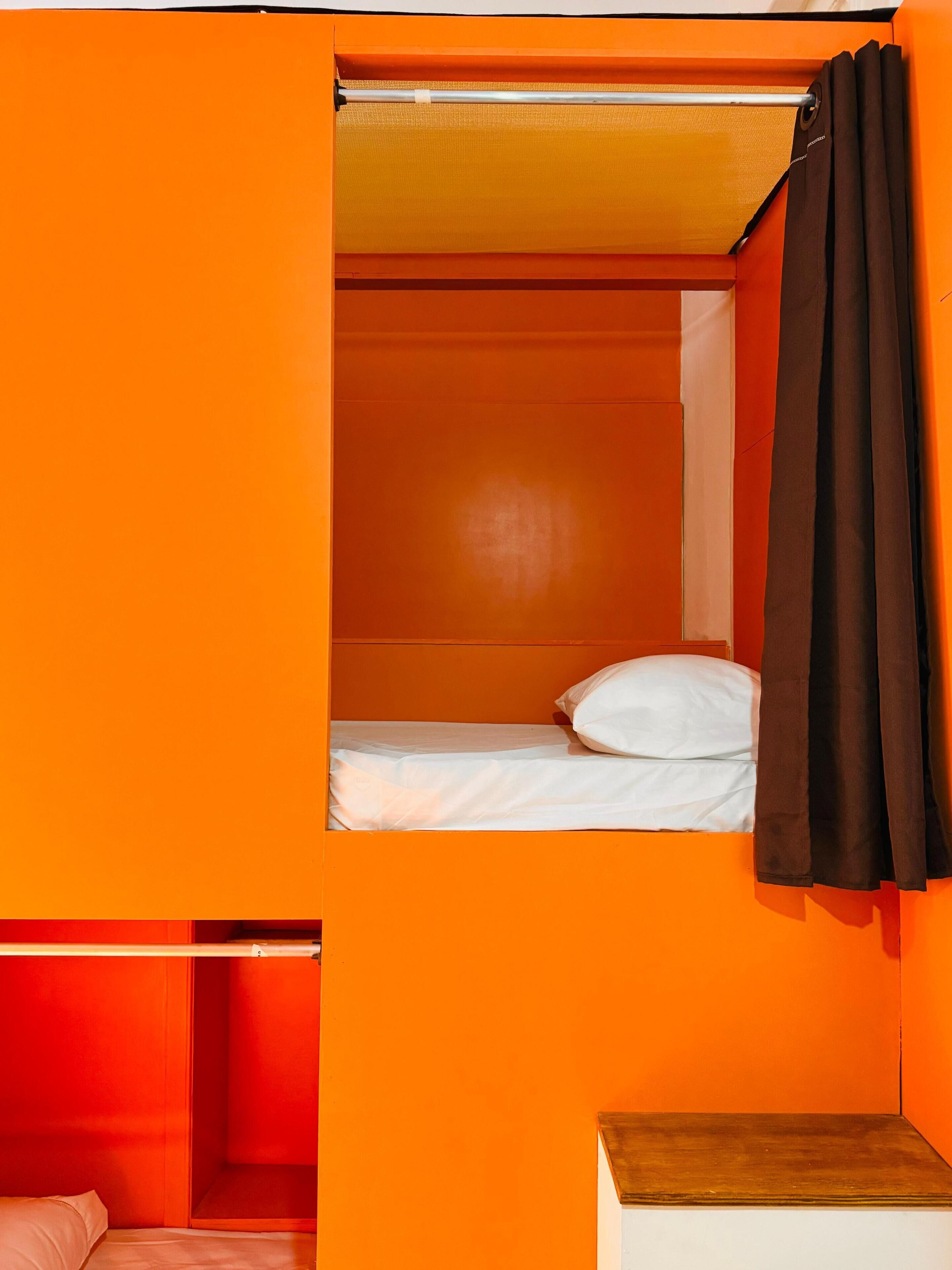Quarto compacto com beliche, uma mesinha de cabeceira e cortina.