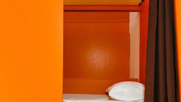 Quarto compacto com beliche, uma mesinha de cabeceira e cortina.