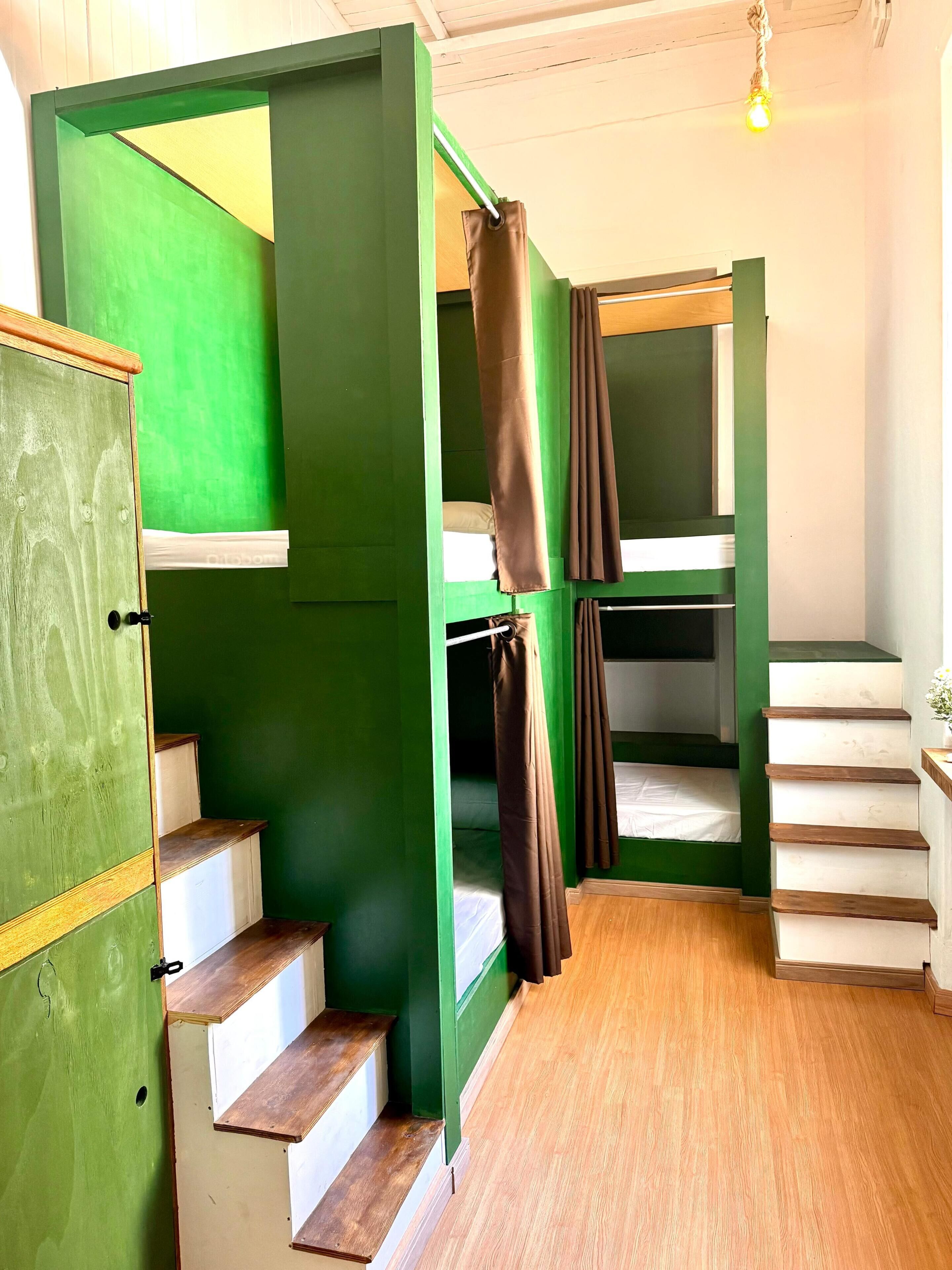A room with bunk beds, wooden stairs, and a green wall.