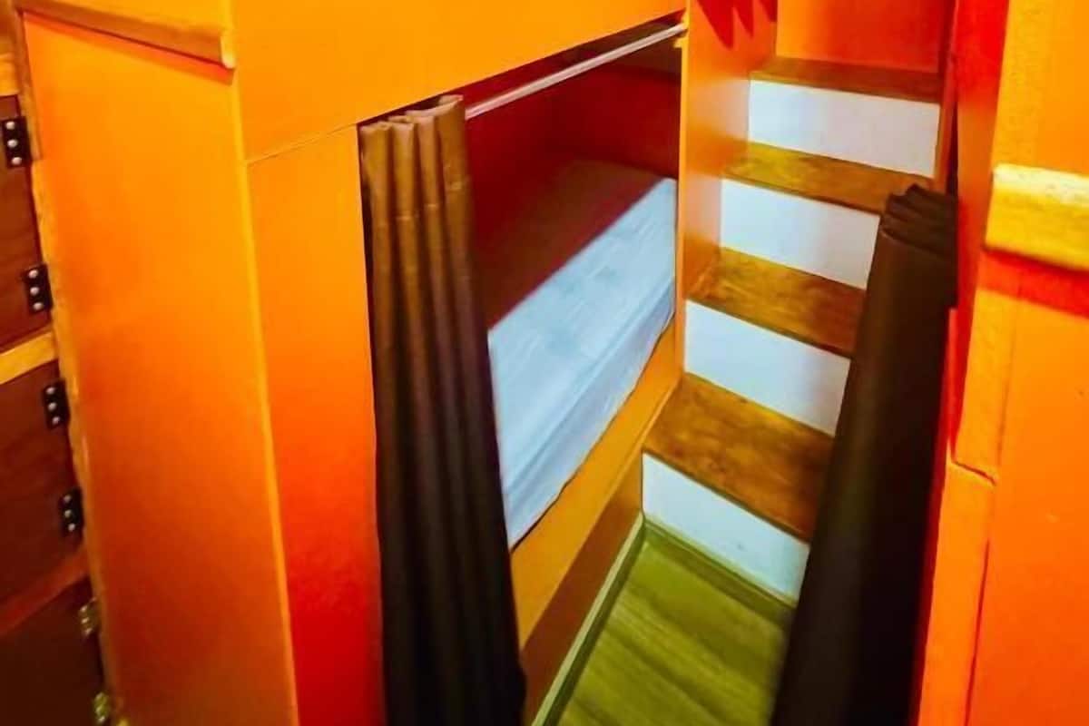 A bunk bed with a mattress and a curtain, a wooden ladder, and a small window.