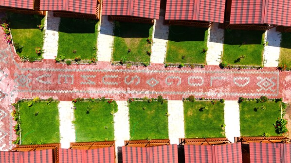 An aerial view of a courtyard with a patterned walkway, green lawns, and red-tiled roofs.