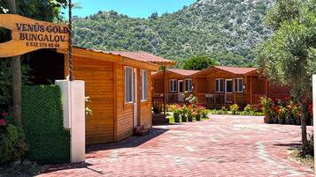 Ein Holzbungalow mit rotem Dach, umgeben von einem gepflasterten Weg und Topfpflanzen.
