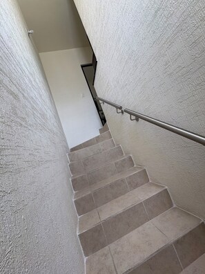 Eine Treppe mit beigen Fliesen und einem Metallgeländer, die zu einer weißen Wand führt.