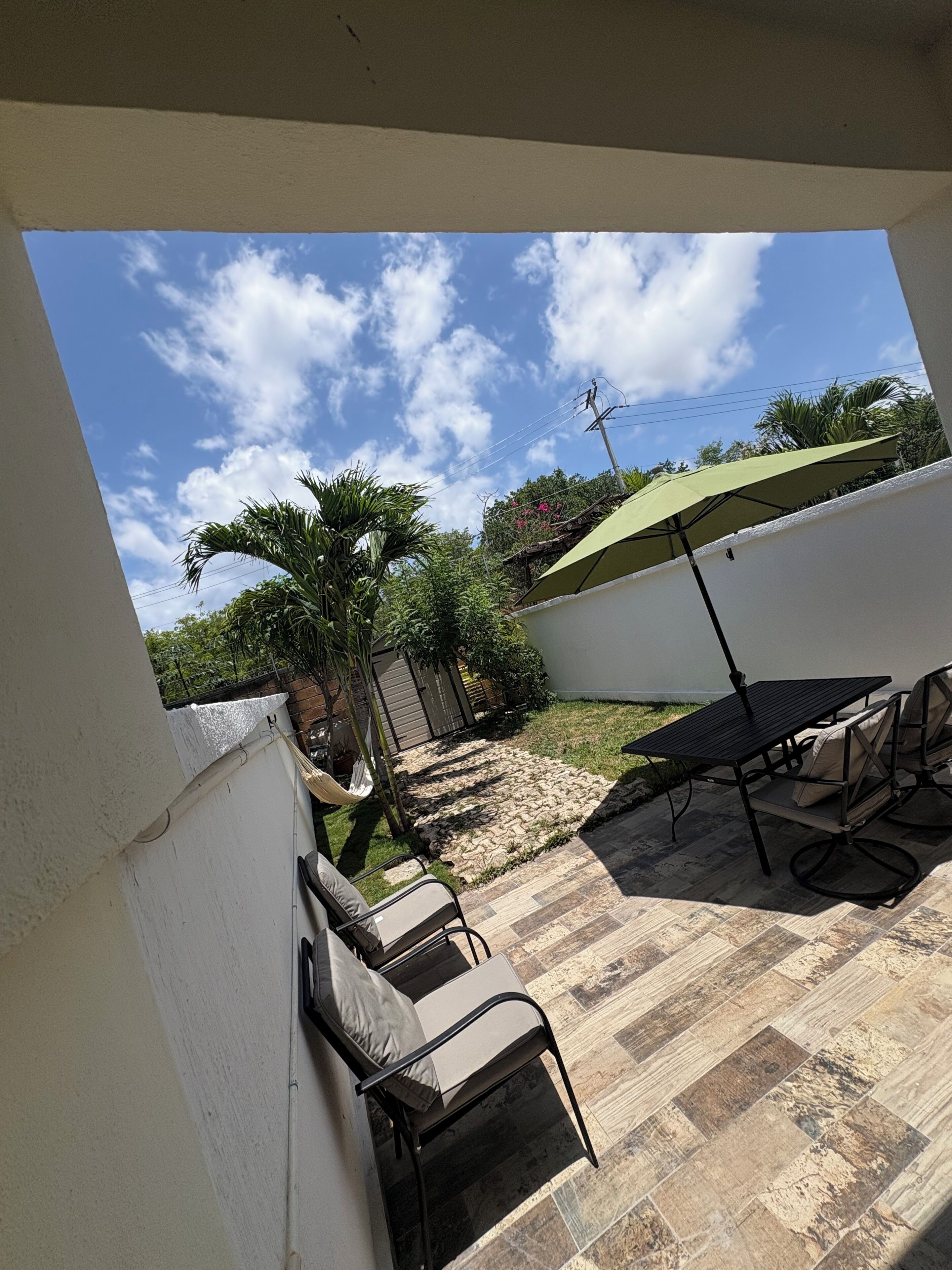 Eine Terrasse im Freien mit Tisch, Stühlen, einer Hängematte und einem grünen Sonnenschirm.