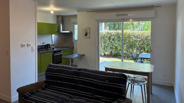 Eine moderne Küche mit grünen Schränken, ein Essbereich mit Tisch und Stühlen und ein Sofa im Wohnbereich.