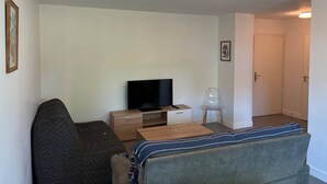 Ein Wohnzimmer mit einer Couch, einem Fernseher auf einem Holzschrank, einem kleinen Tisch und einer Tür zu einem anderen Raum.
