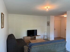 Ein Wohnzimmer mit einer Couch, einem Fernseher auf einem Holzschrank, einem kleinen Tisch und einer Tür zu einem anderen Raum.