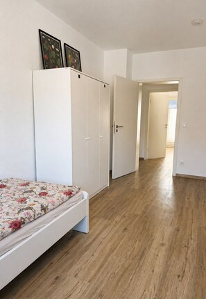 Ein Schlafzimmer mit Bett, Kleiderschrank und einem zur anderen Kammer führenden Flur.