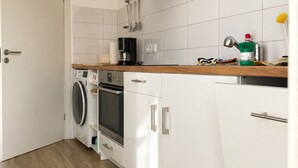 Eine kompakte Küche mit Waschmaschine, Backofen und Kaffeemaschine.
