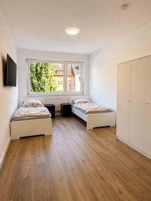 Ein Schlafzimmer mit zwei Betten, einem Fenster, einem Kleiderschrank und einer Deckenleuchte.