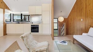 Una cocina moderna con armarios blancos, horno empotrado y comedor con mesa de vidrio y sofá blanco.