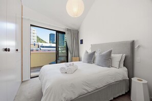 Hotellihuone, jossa on sänky, yöpöytä, lamppu, näkymä ulos ja liukuovi.
