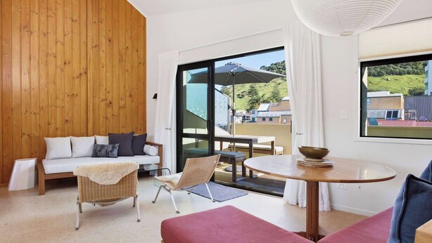 Una habitación moderna con pared de madera, un sofá, una silla, una mesa y un gran ventanal con vistas a edificios y colinas.