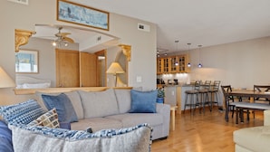 A living room with a sofa, a dining area with chairs, a kitchen with cabinets, and a ceiling fan. - Ocean & Lake View |3BR |Steps to Beach & Boardwalk (Carolina Beach)