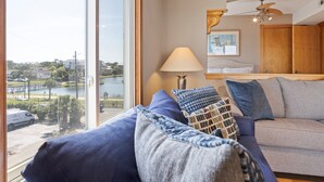 A room with a large window, a sofa, a lamp, and a ceiling fan. - Ocean & Lake View |3BR |Steps to Beach & Boardwalk (Carolina Beach)