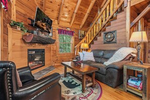 Ein gemütliches Blockhaus-Interieur mit Kamin, Holzwänden, einer Couch, einem Couchtisch und einer Treppe.