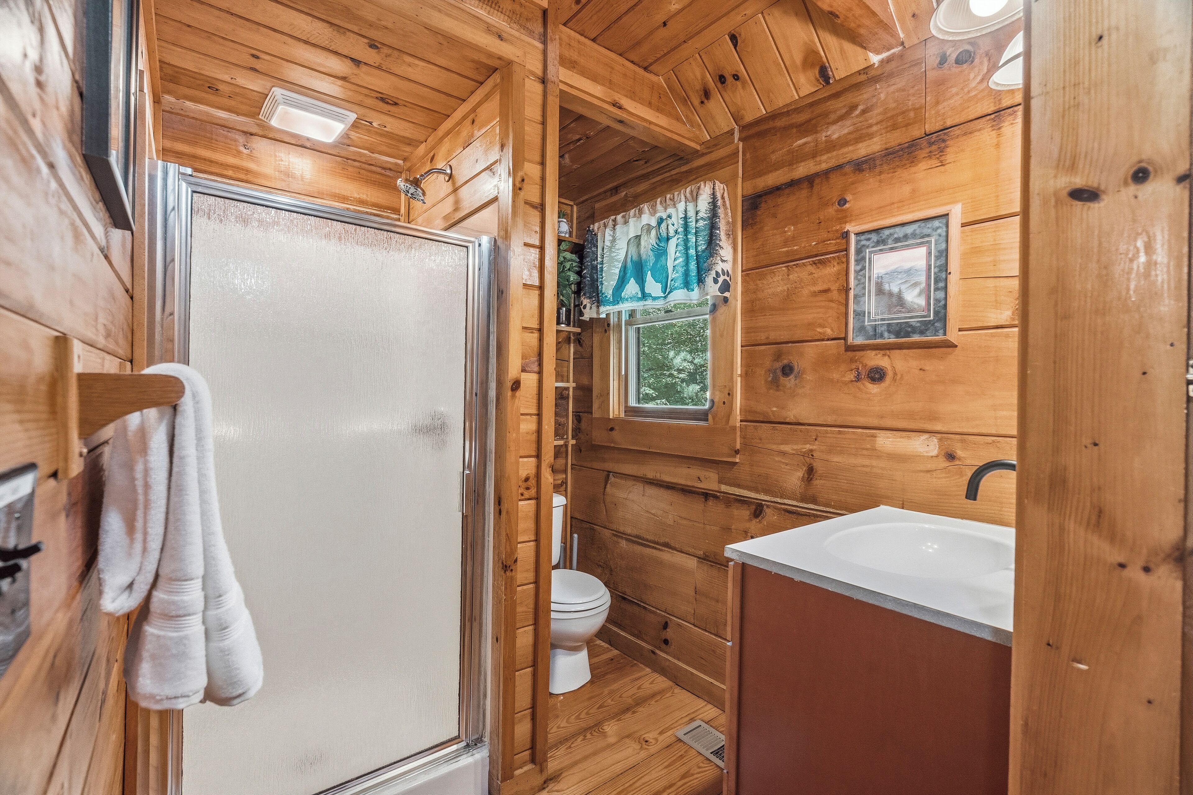 A wooden cabin bathroom with a shower, toilet, and sink.