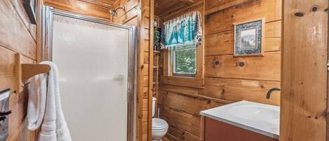 A wooden cabin bathroom with a shower, toilet, and sink.