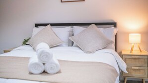 Un lit bien fait, avec des serviettes pliées, une lampe de chevet et une citation encadrée accrochée au mur.
