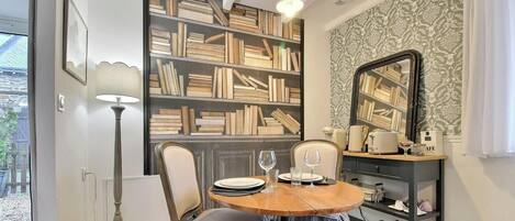 A dining area with a round table, chairs, a bookshelf, a mirror, and a window.