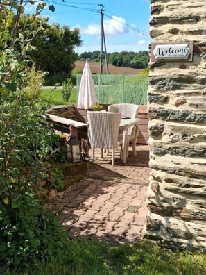 A patio with wicker furniture, a welcome sign, and a stone wall. - Le Petit Cottage - RUFFIAC (RUFFIAC)