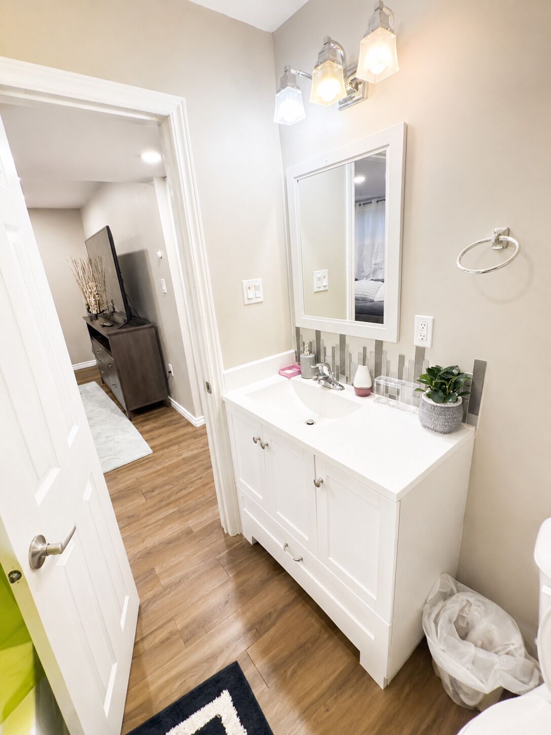 A bathroom with a white vanity, a mirror, a towel ring, and a potted plant.