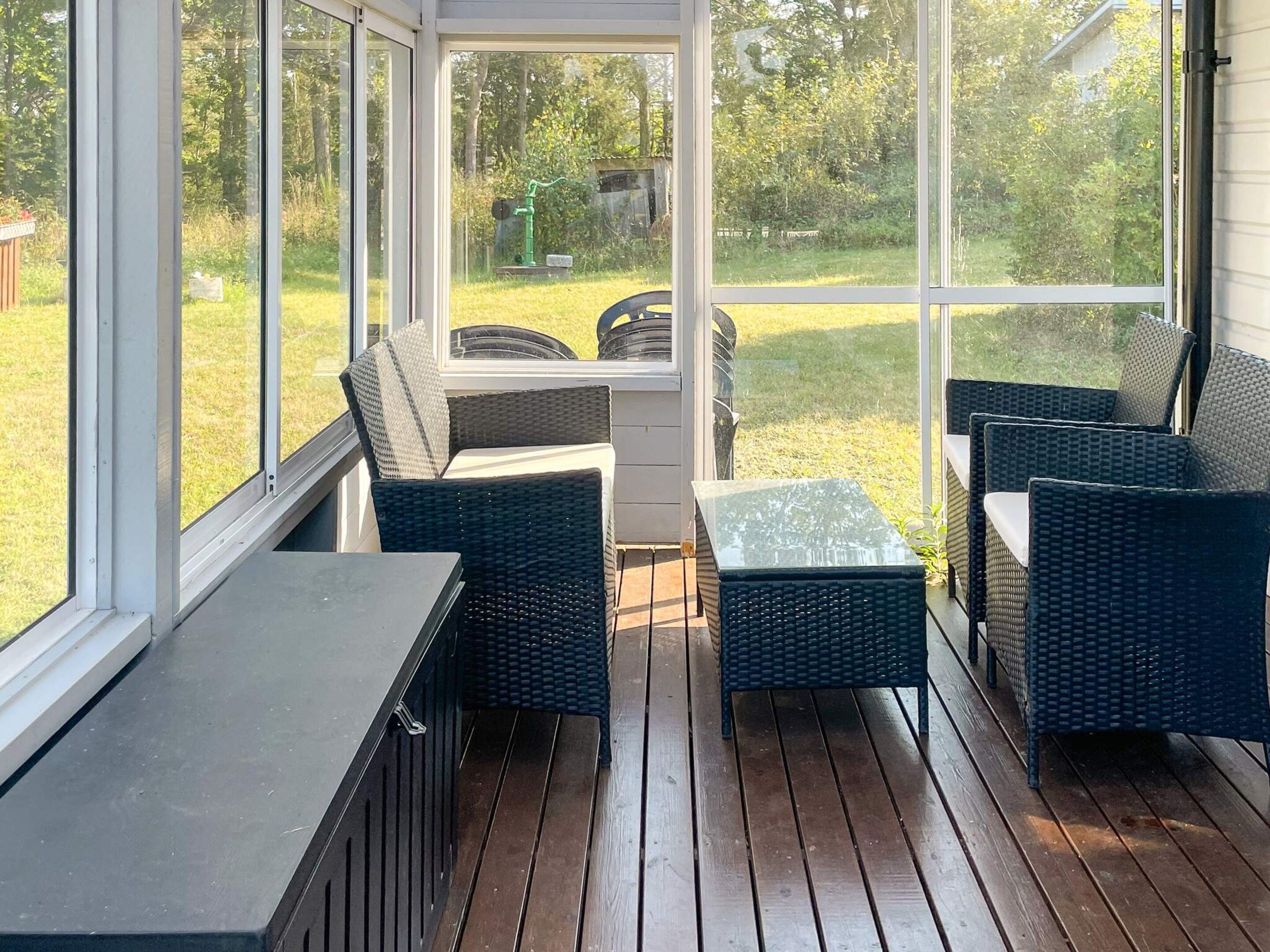 A covered outdoor patio with wicker furniture and a glass table.