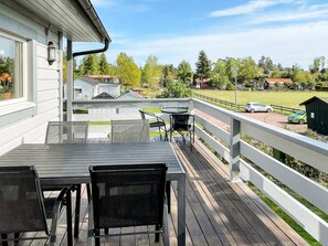 A wooden deck with a table and chairs, overlooking a residential area with houses and a green field. - 7 Person Holiday Home in Monsteras (Monsteras)