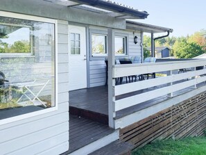 A covered outdoor deck with a railing, a door, and a window overlooking a grassy area. - 7 Person Holiday Home in Monsteras (Monsteras)