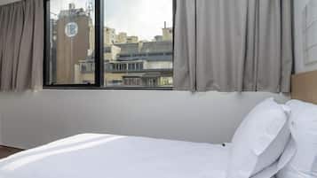 Habitación de hotel con cama, ventana con cortinas y vista a edificios.