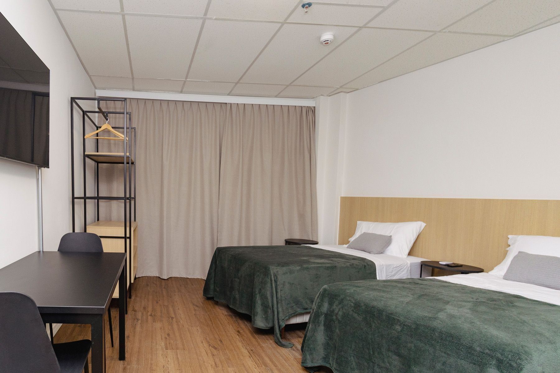A hotel room with a desk, two beds, a wardrobe, and a television.