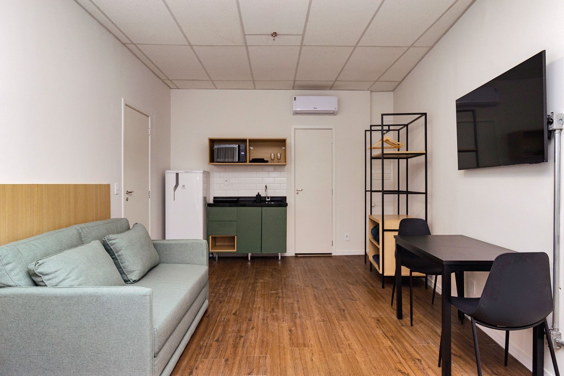 Un espacio habitable compacto con kitchenette, un sofá, una mesa de comedor con sillas y un televisor montado en la pared.