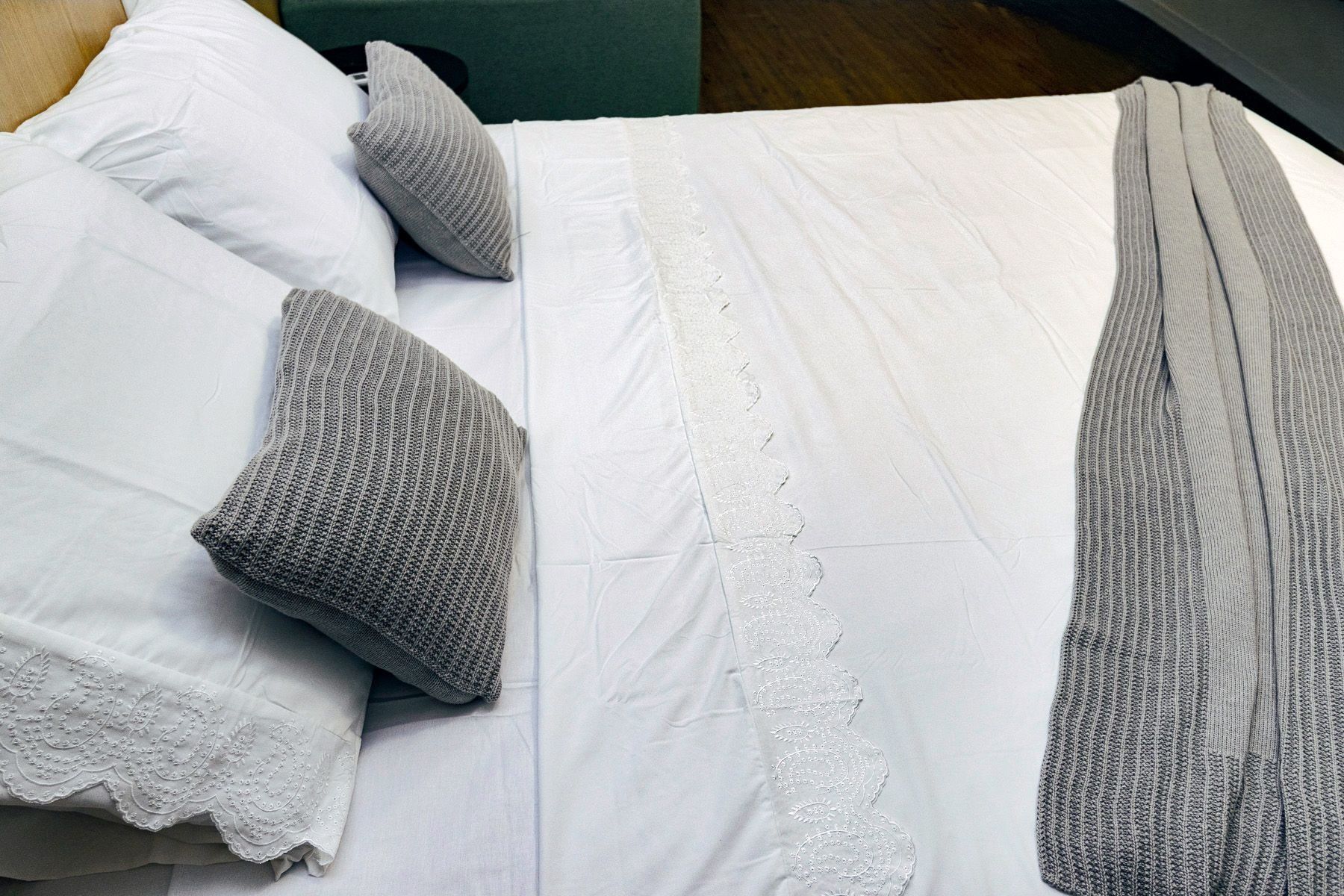 Un letto con biancheria bianca, cuscini grigi e una coperta grigia.