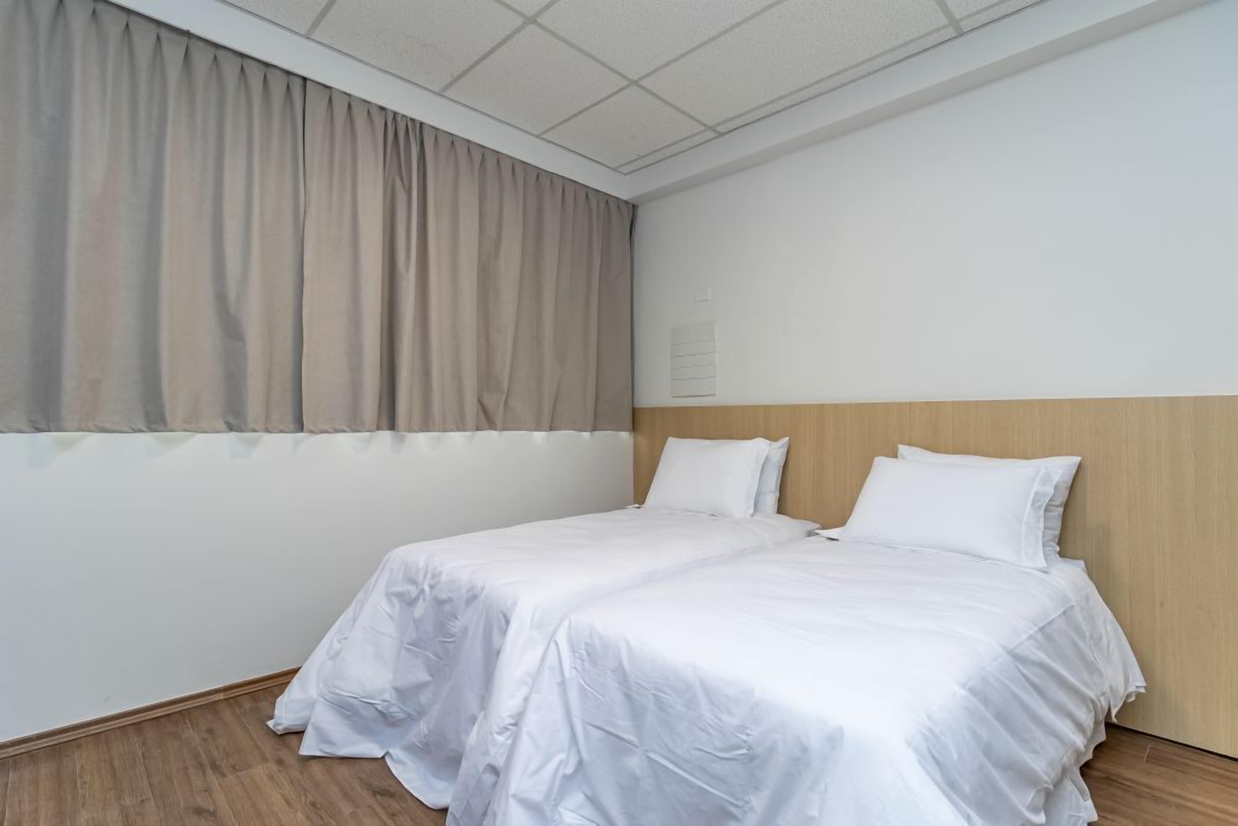 A single bed with white bedding in a room with a wooden headboard, beige curtains, and a tiled ceiling.