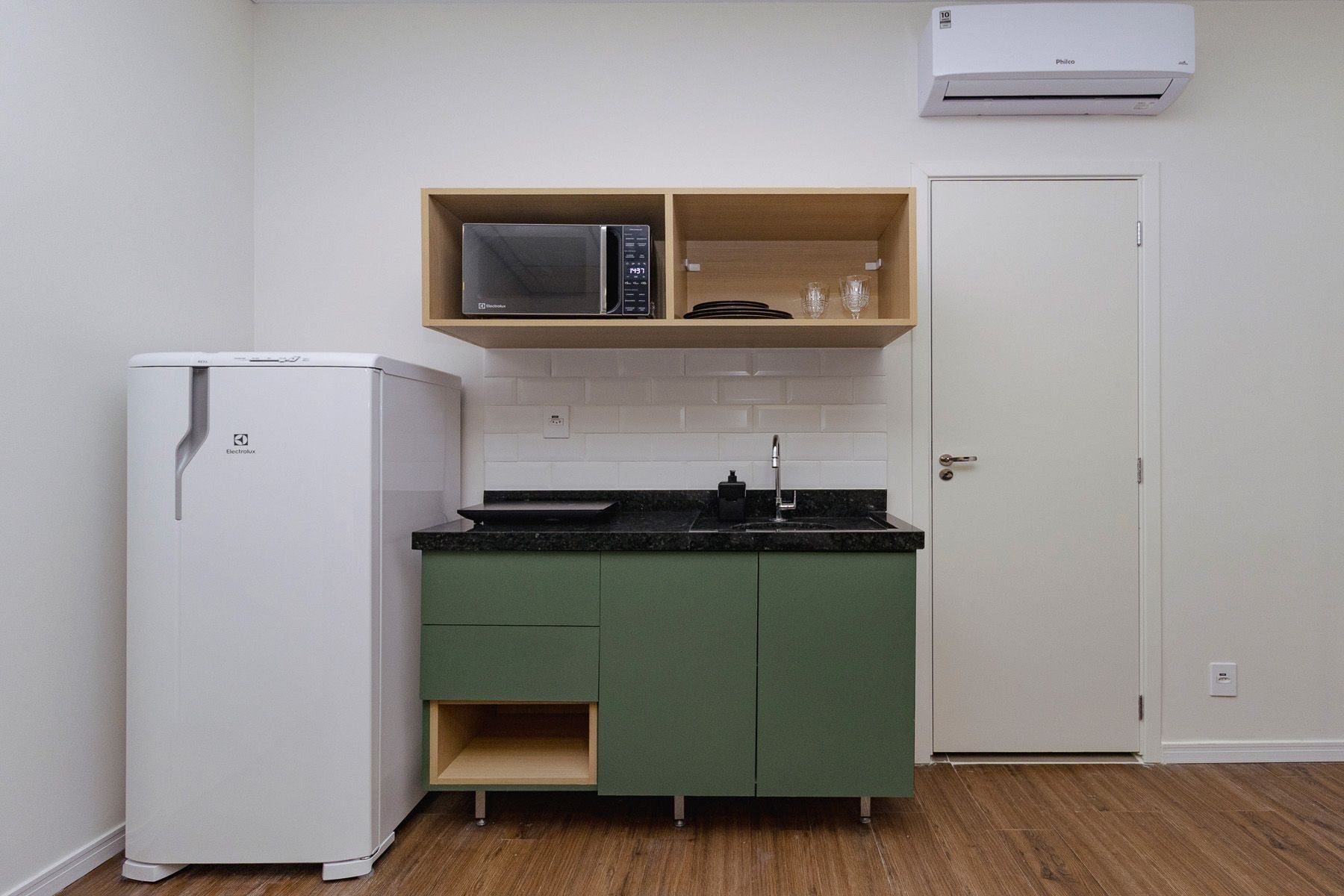 A compact kitchen with a white refrigerator, a microwave, and a sink with a green cabinet.