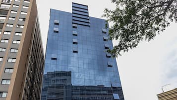 Un edifici modern alt amb façana de vidre, entrada a nivell del sòl i zona d'aparcament amb cotxes.