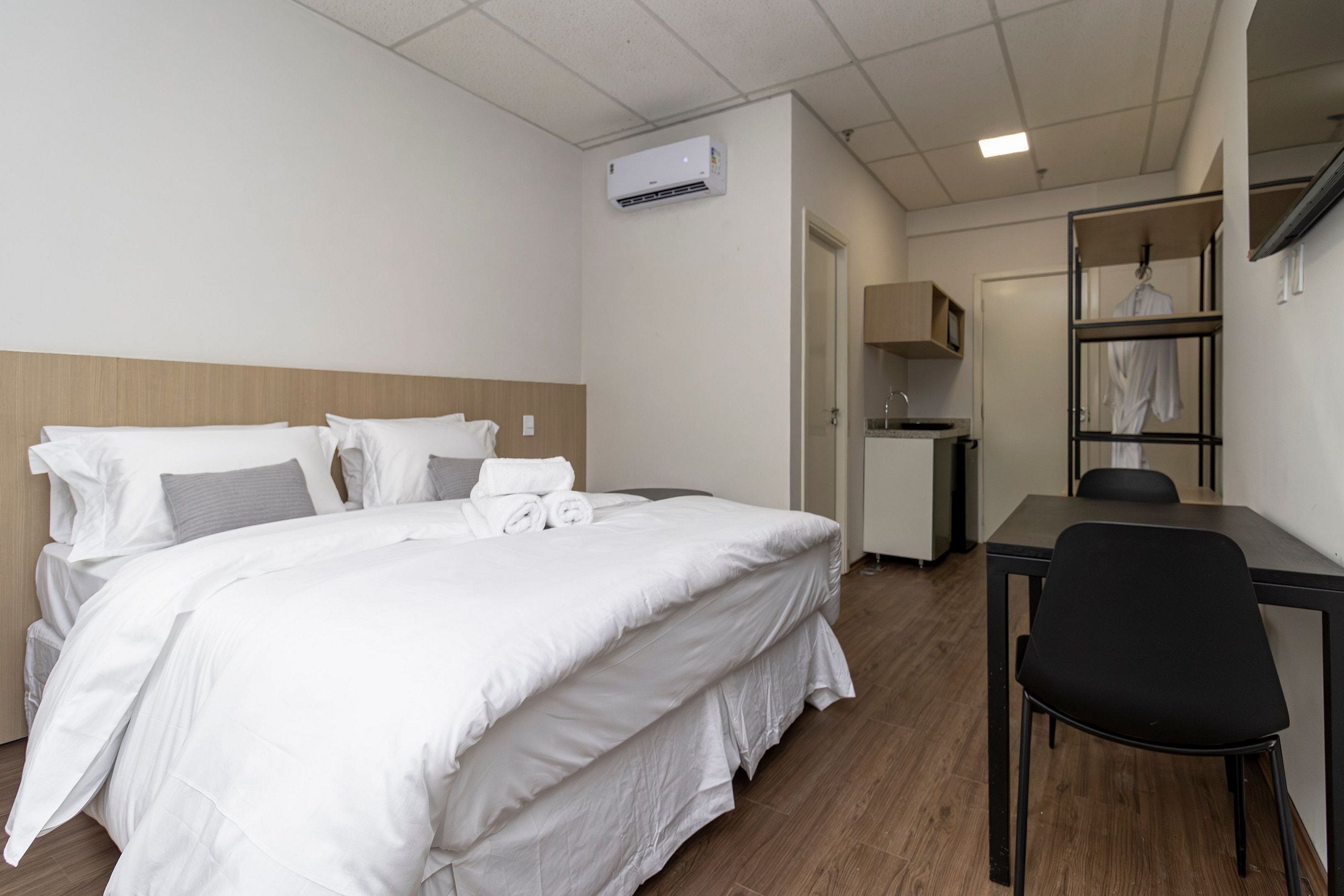 A hotel room with a bed, a desk, a chair, an air conditioning unit, and a wardrobe.