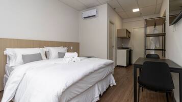 A hotel room with a bed, a desk, a chair, an air conditioning unit, and a wardrobe.