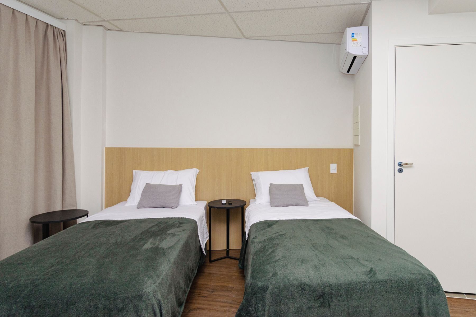 Een hotelkamer met twee bedden, een nachtkastje, een airconditioning en een deur.