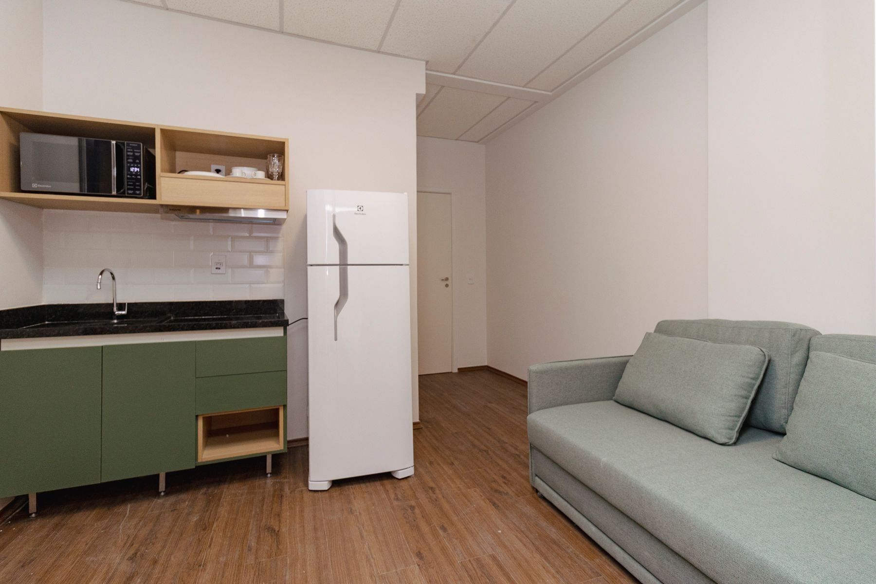 Eine kleine Küche mit Mikrowelle, Kühlschrank und grünen Schränken.