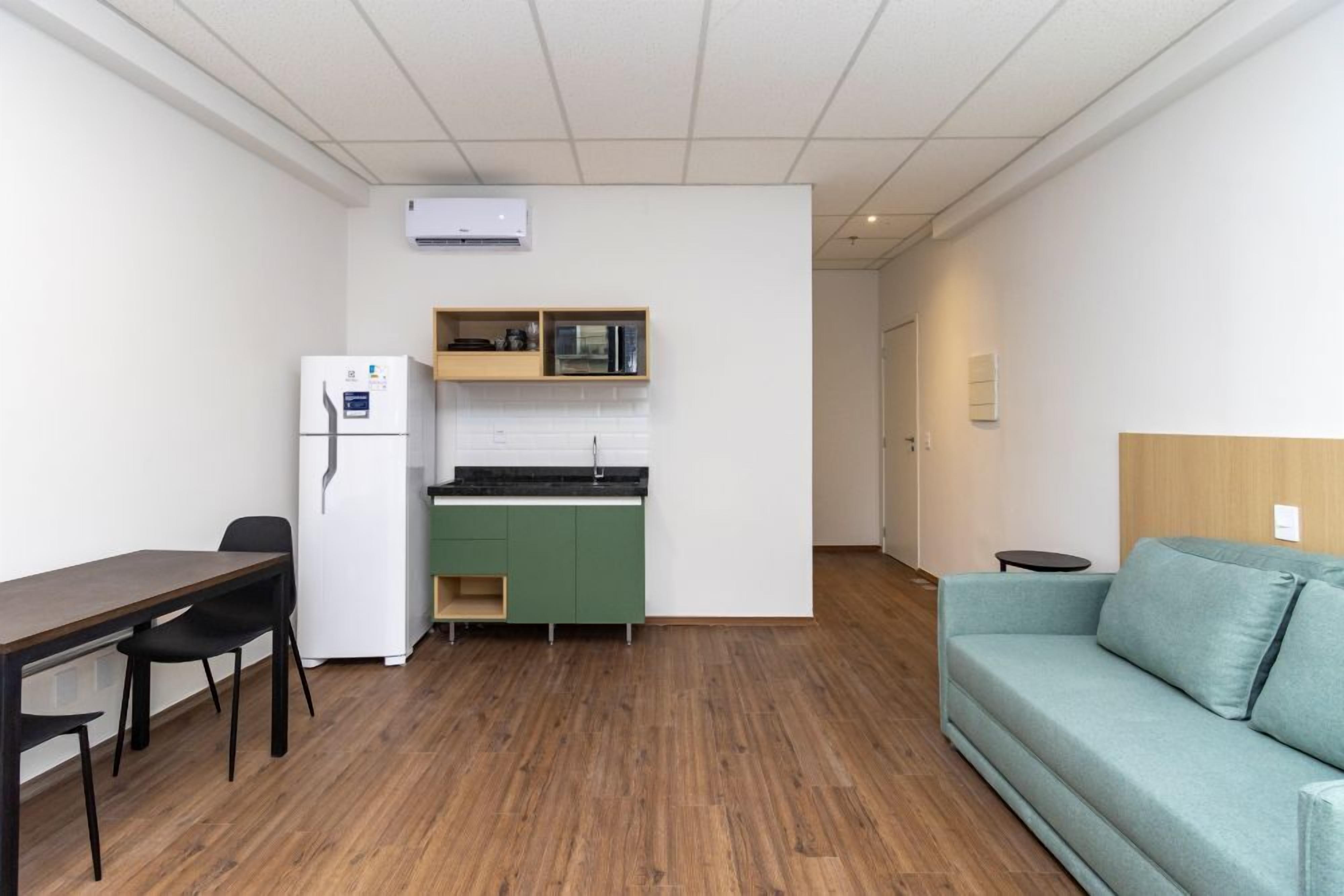 Un espacio habitable compacto con kitchenette, una mesa de comedor con sillas, un sofá y una pequeña mesita auxiliar.
