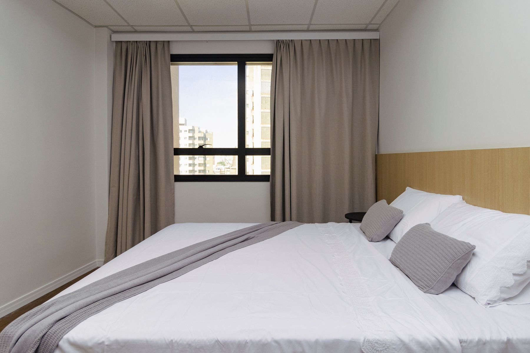 Una habitación de hotel con cama, cortinas, ventana y vista a edificios.