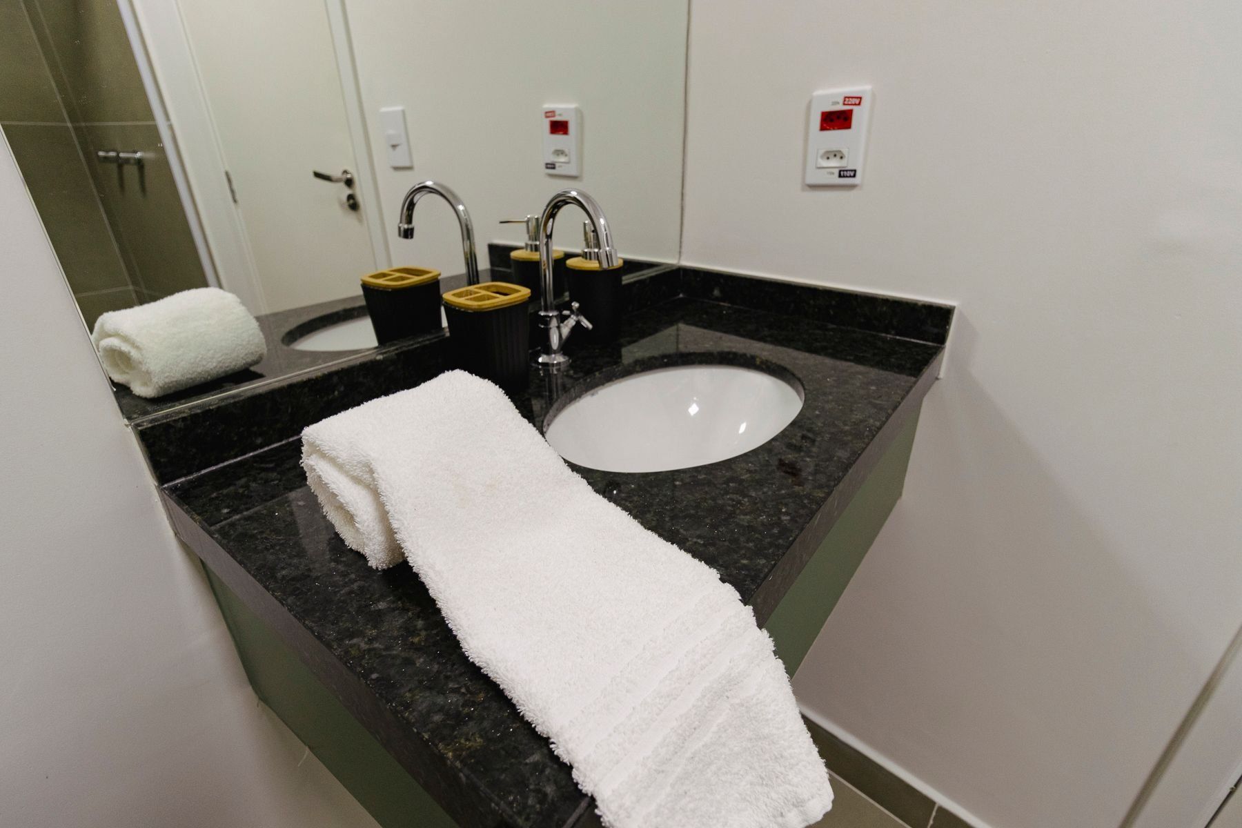 A bathroom with a white sink, two faucets, a towel, and a mirror.