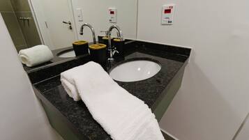 A bathroom with a white sink, two faucets, a towel, and a mirror.