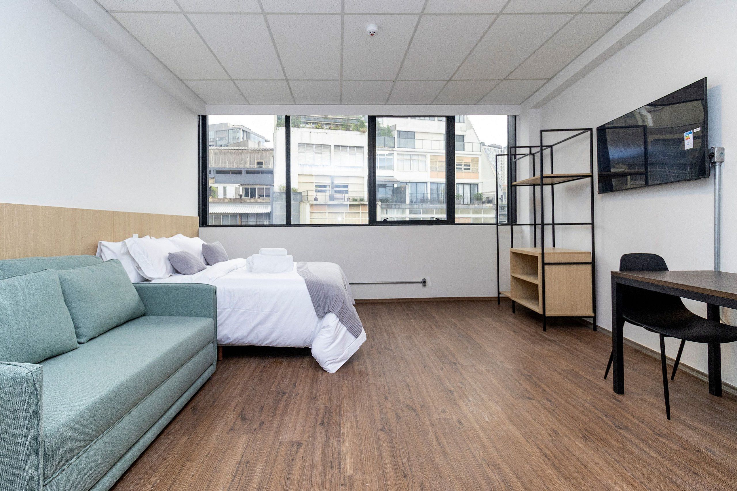 A hotel room with a bed, a sofa, a desk, and a TV.