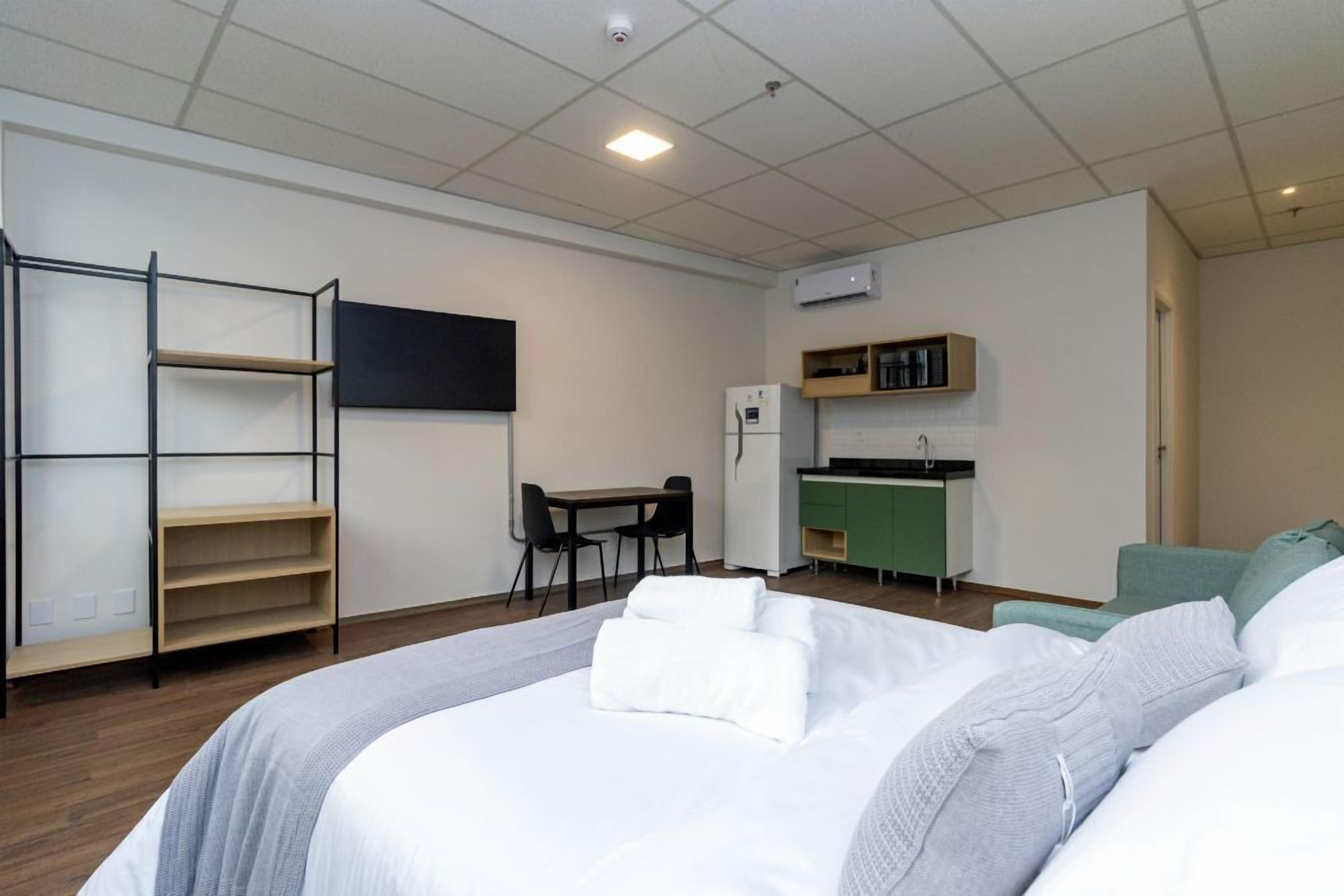 Une chambre d’hôtel comprenant un lit, un bureau, une chaise, une kitchenette et une armoire.